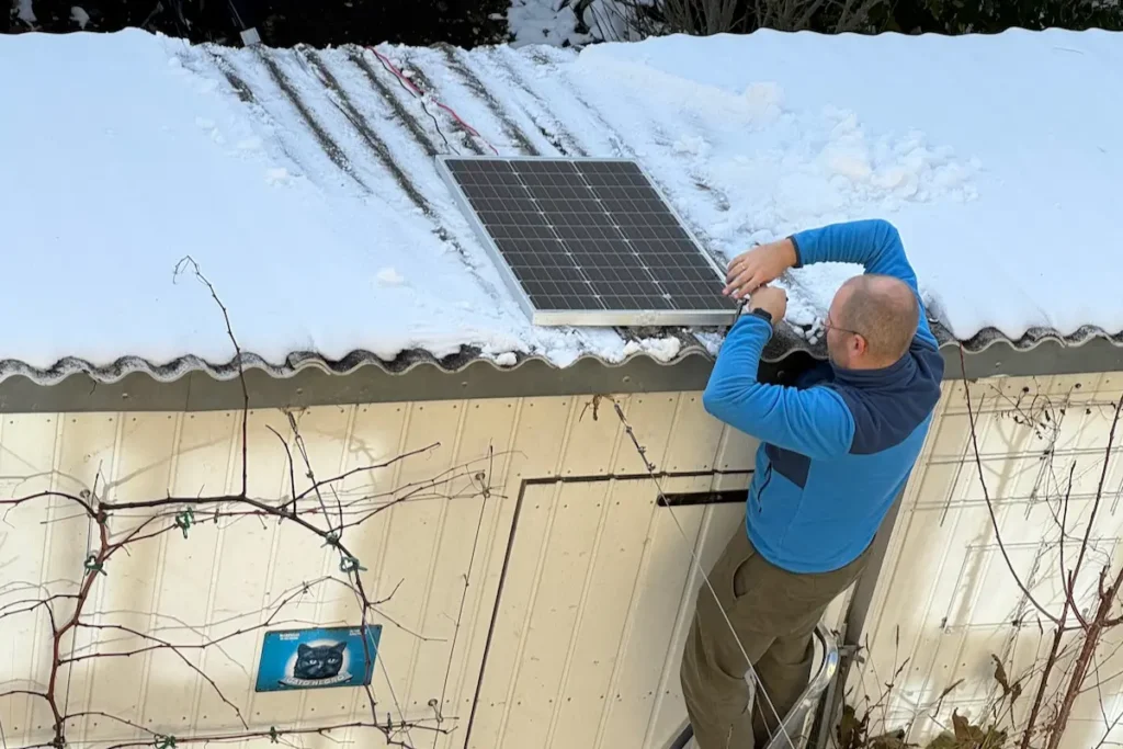 Mann steht auf Leiter und verschraubt Solarzelle auf einem Dach