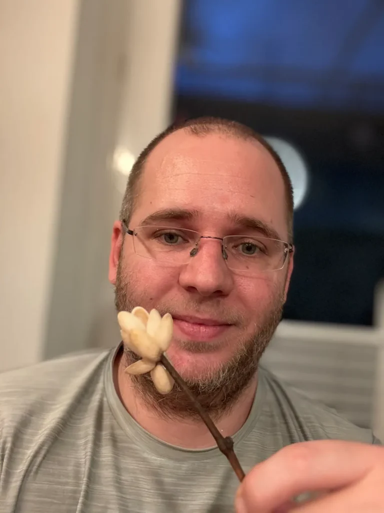 Selfie von Mann mit Ast in der Hand an dem eine Blüte aus leeren Pistazienschalen geklebt ist.